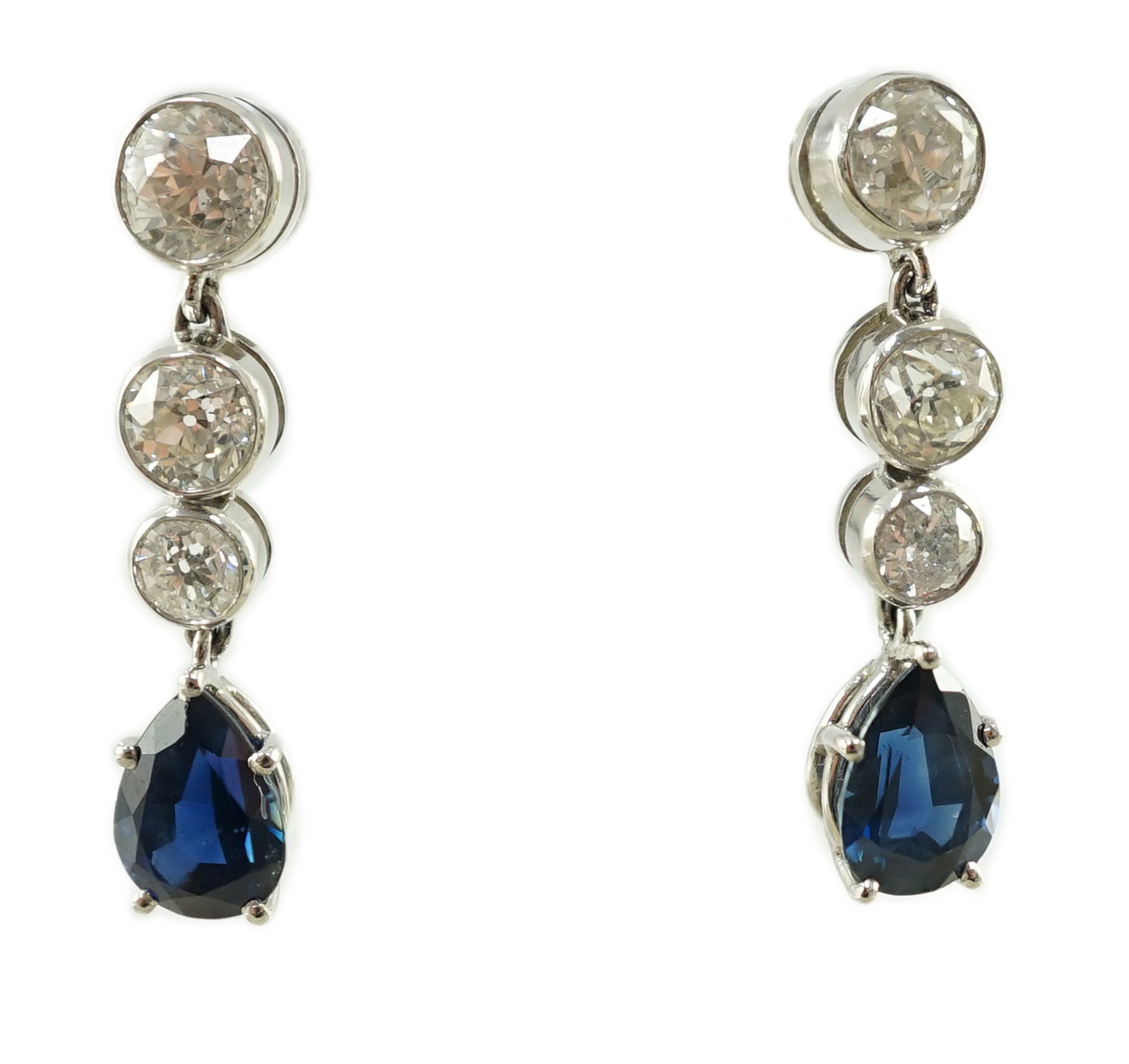 A pair of 1980's platinum, single stone pear cut sapphire and graduated three stone collet set diamond drop earrings